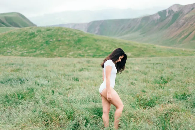 Model in a white bodysuit looking down in a green meadow.