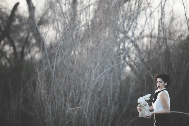 Black-and-white portrait of a model holding fabric among bare branches.