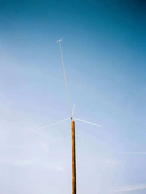 Tall, slender pole and fine wires against a pale blue sky.