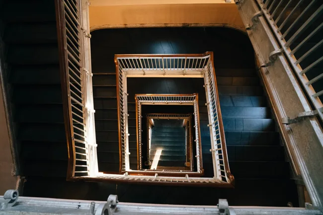 View down through the repeating rectangular turns of a stairwell.