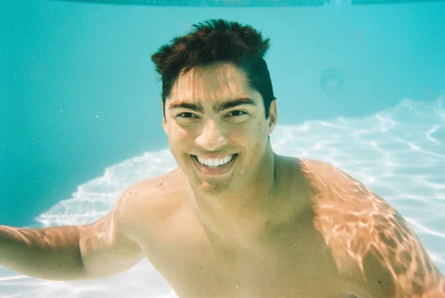 Smiling man in turquoise swimming-pool water.