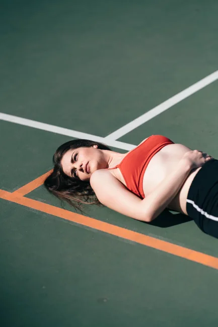 Woman in a red athletic top reclining on a green court.