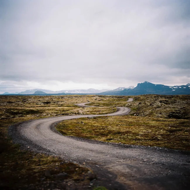 A winding road crossing open mossy terrain beneath heavy clouds.