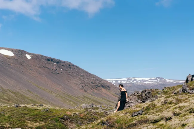 Wide landscape with a model standing beneath a clear blue mountain sky.