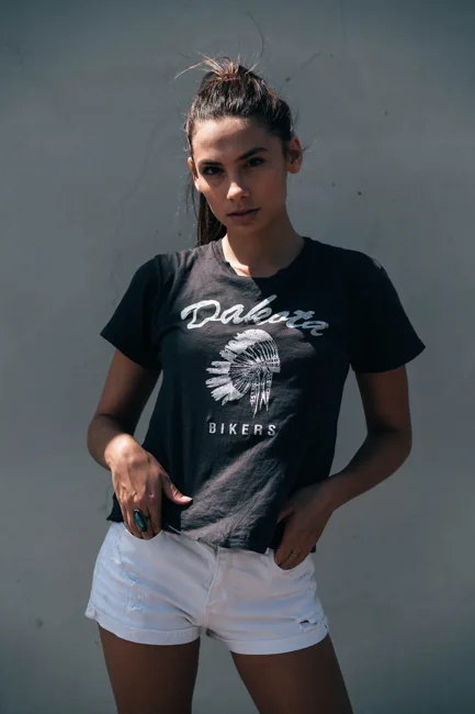 Woman in a black graphic T-shirt and white shorts against a gray wall.