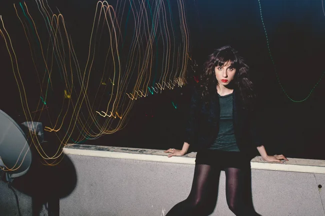 Model standing beside a railing beneath curved trails of light.