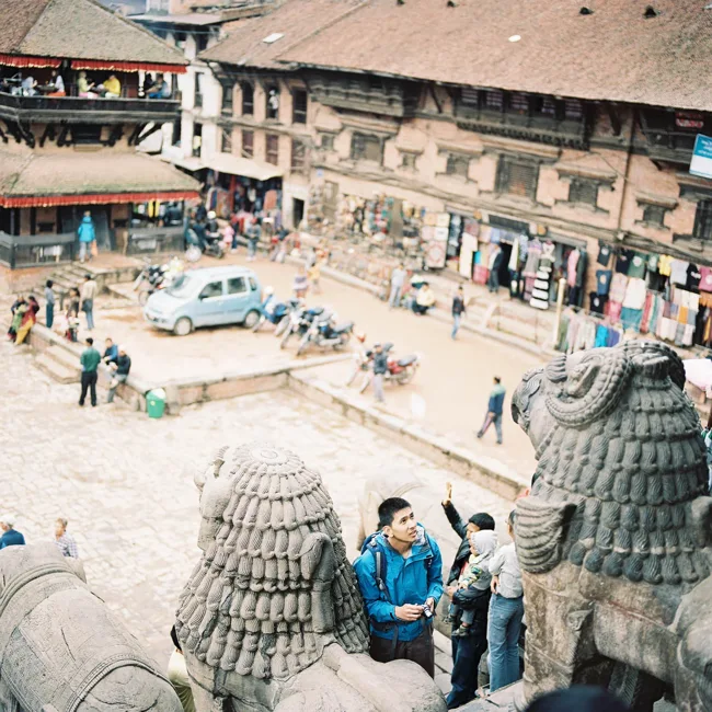 View down into a busy square framed by carved stone figures.