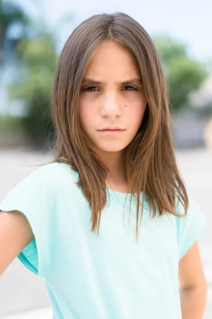 Close outdoor portrait of a woman in a pale blue shirt.