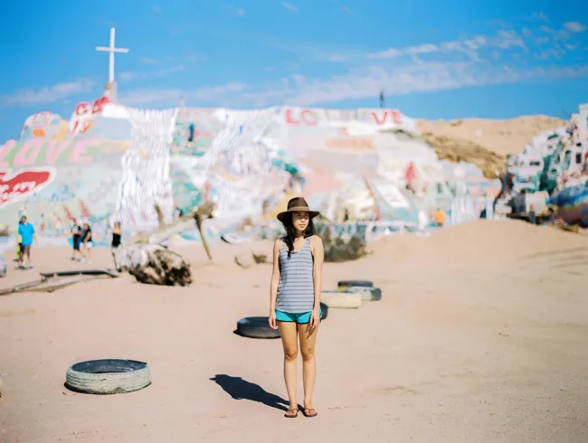 Traveler standing in front of the colorful painted slopes of Salvation Mountain.