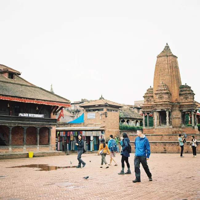 People crossing a brick square surrounded by temples in Nepal.