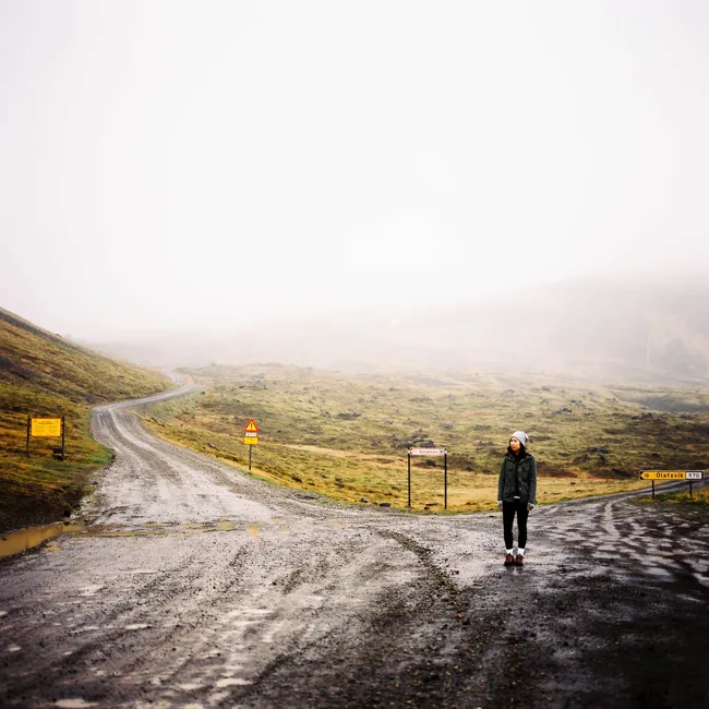 Traveler standing on a wet road winding into mountain fog.