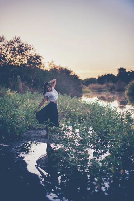 Model standing near water amid dense green vegetation.