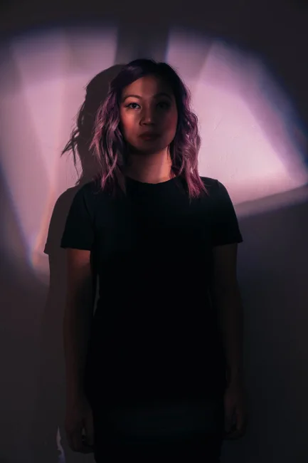 Model in a black shirt framed by soft purple light and shadow.