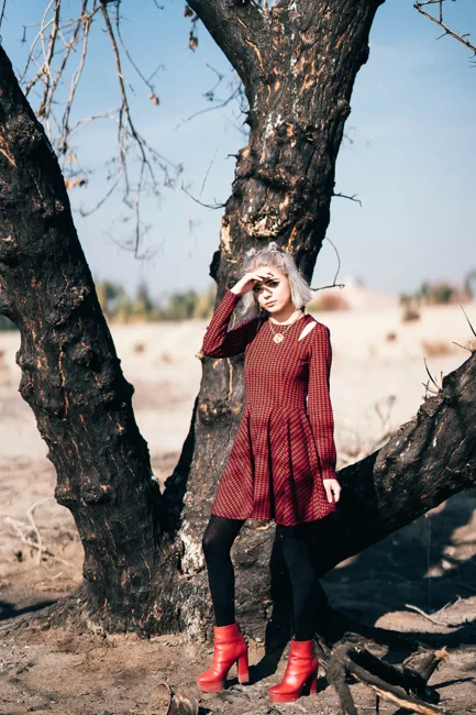 Model in a burgundy coat standing against a large tree.