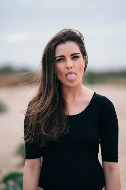 Close portrait of a model playfully sticking out her tongue outdoors.