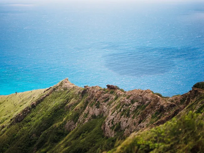 Steep green crater ridge above the deep blue ocean.