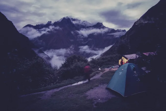 Tent pitched beneath dramatic mountains in low evening light.