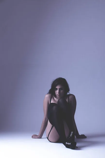 Model seated on a studio floor in soft violet light.