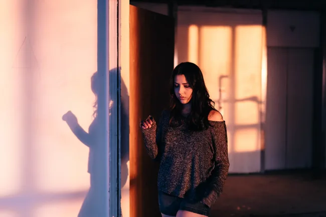Model beside a doorway casting long shadows on a sunlit wall.