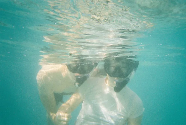 Underwater view of a swimmer beneath a sunlit turquoise surface.