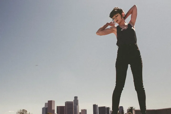 Model in black posing on a rooftop with arms raised.