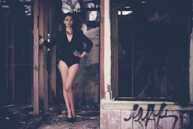 Model in black standing in the doorway of a weathered building.