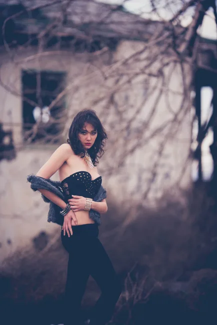 Model holding a jacket against her chest among bare branches.