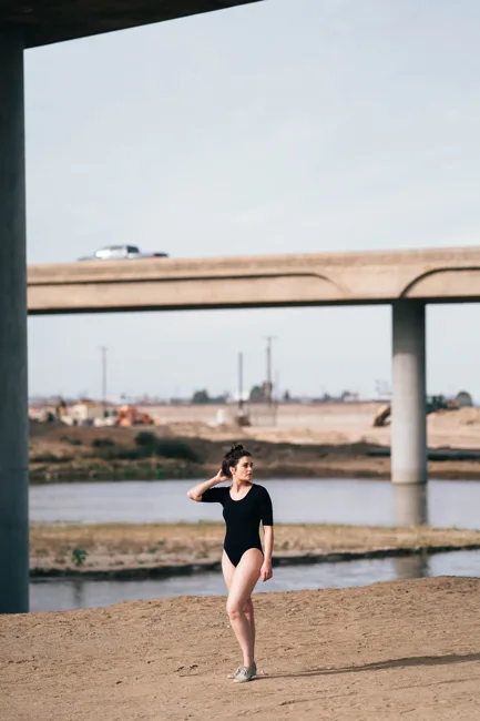 Model in a black bodysuit standing beneath a concrete overpass.