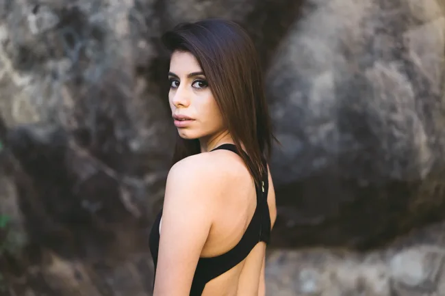 Woman in black looking over her shoulder beside a rock face.