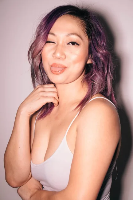 Model with purple hair smiling in a pale tank top.