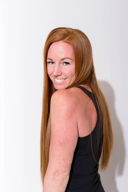 Red-haired woman smiling over her shoulder in a black top.