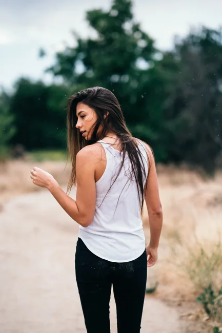 Woman in a white tank top looking back along a path.