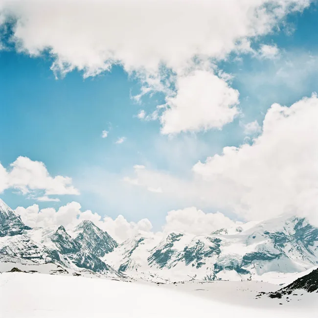 Snow-covered Himalayan peaks beneath bright blue sky and clouds.