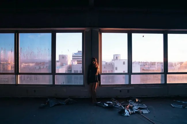 Model silhouetted beside a long row of windows in an empty room.