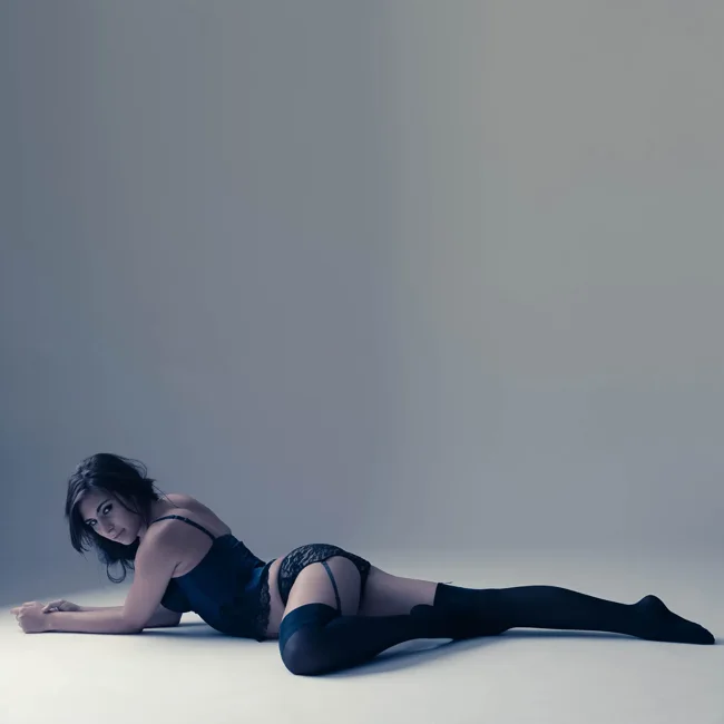 Model reclining across a gray studio floor in black clothing.