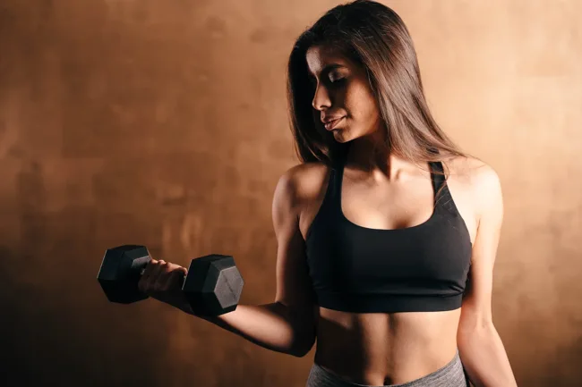 Woman lifting a dumbbell in warm directional light.