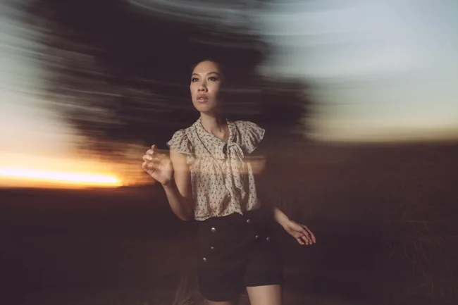 Model in a patterned top surrounded by blurred evening light.