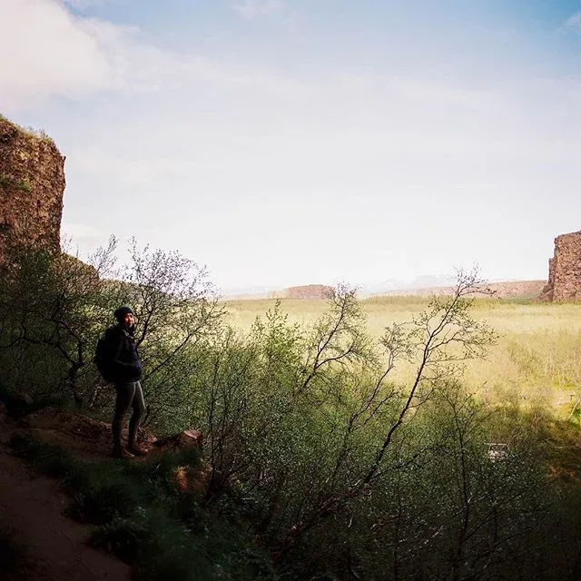Figure beside a rock wall looking out across a sunlit landscape.
