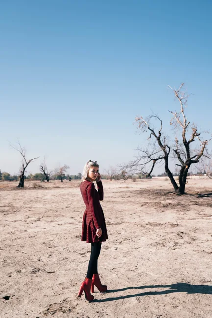 Model in a burgundy coat and red boots in a dry landscape.