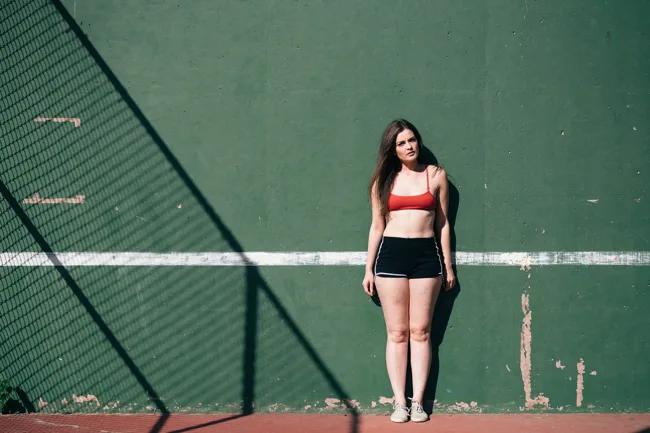 Woman in athletic clothing standing against a green court wall.