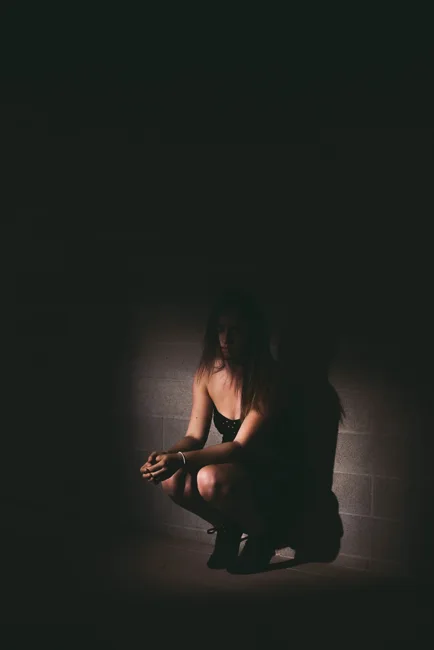 Seated model illuminated by a small pool of light in darkness.