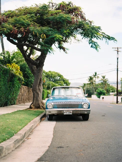 Vintage car parked on a quiet, tree-lined tropical street.