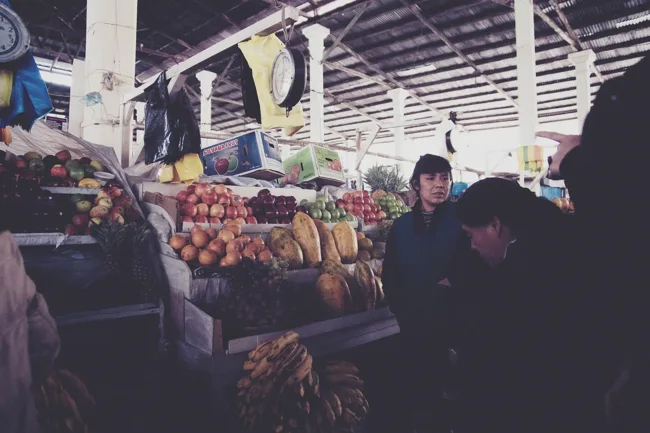 People passing a fruit stall inside a crowded market.