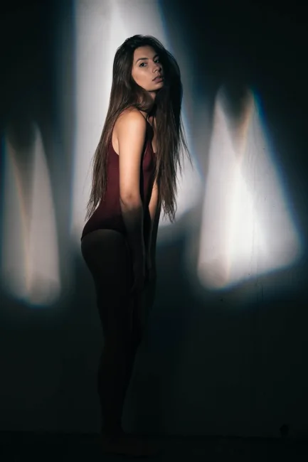 Model in dark clothing standing in narrow bands of light and shadow.
