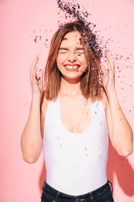 Woman smiling as confetti falls against a pink background.