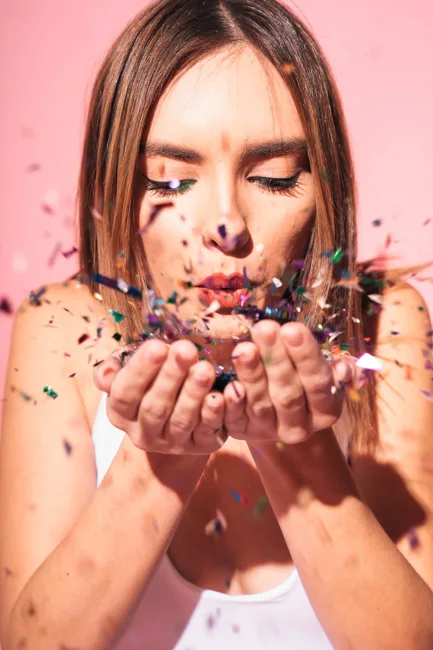 Close portrait of a woman blowing colorful confetti from her hands.